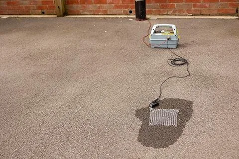 Radiodetection Earth Mat connected to a transmitter on a paved driveway near a brick wall.
