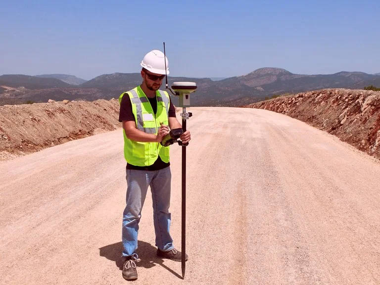 Technician using a GNSS GPS rover pole to capture real-time coordinates while locating utilities on a dirt road.