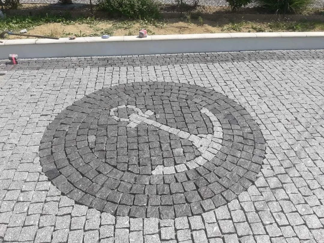 Pictogramme de stationnement de handicap peint sur un pavé de rue en pierre, avec bordures en béton en arrière-plan.
