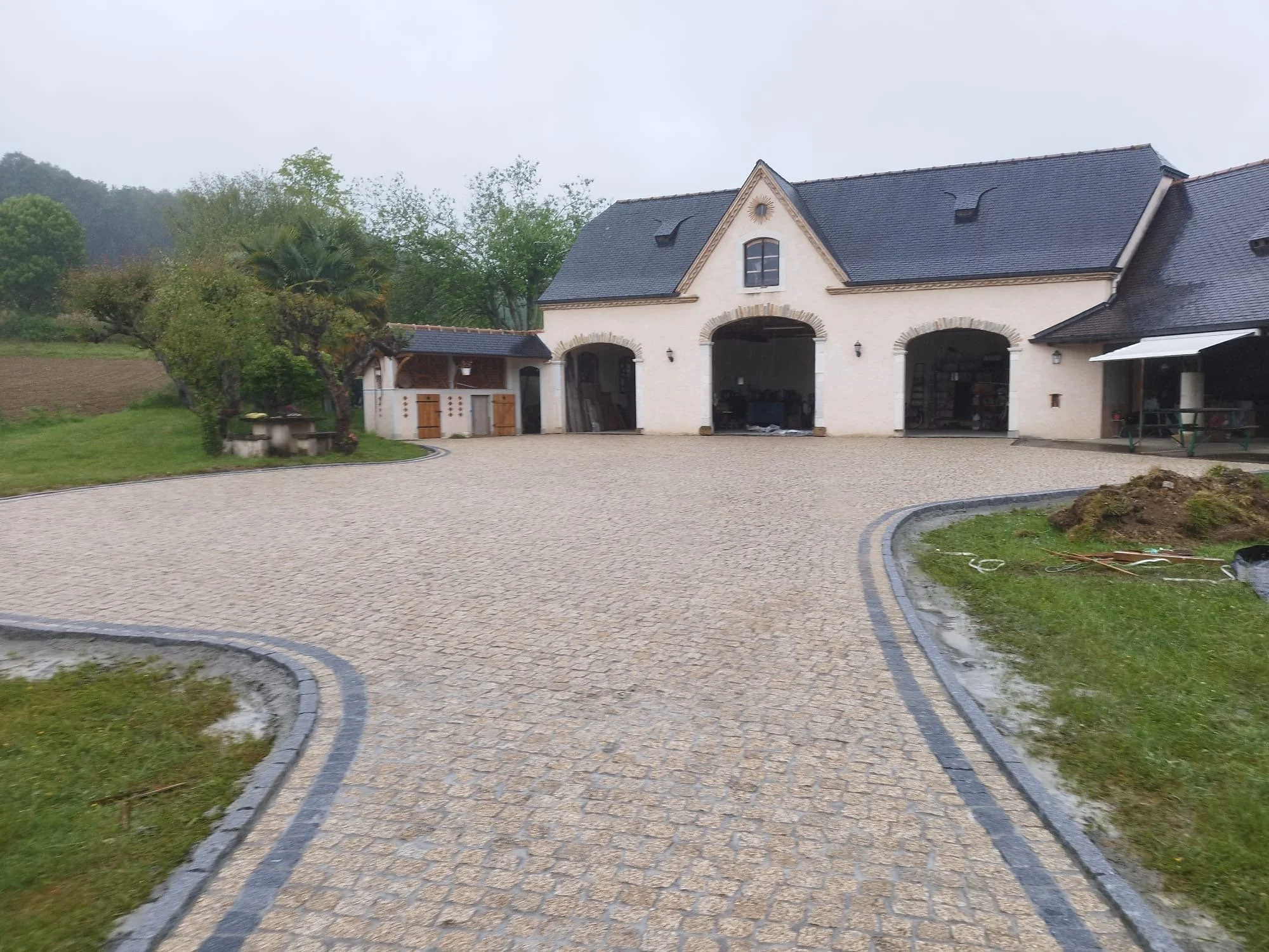 Maison avec un toit en ardoise et une façade en pierre, entourée d'arbres verts et d'une allée pavée