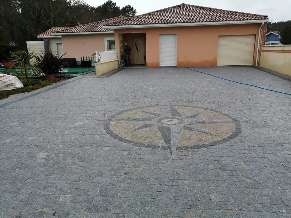 Une cour pavée en pierre avec un motif de compas au centre et une maison en arrière-plan.