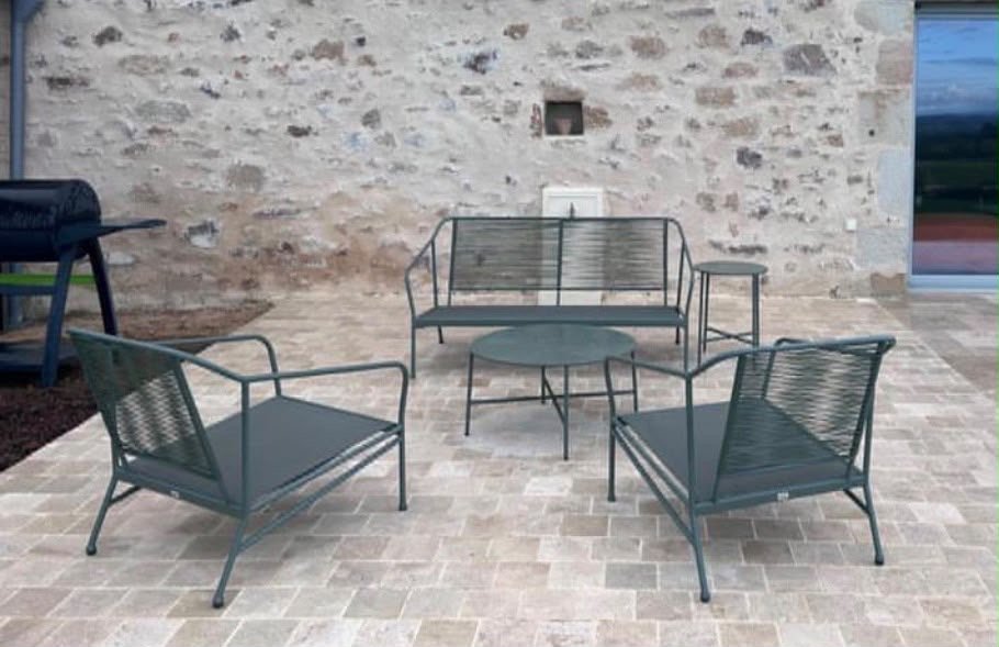 Mobilier de patio avec une table ronde, trois fauteuils et un banc en métal, avec un mur en pierre en arrière-plan.