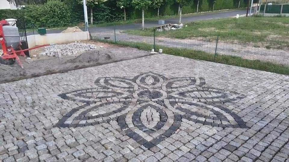 Chemin de pavés avec un motif géométrique noir et blanc au centre, entouré d'une zone en construction et d'un grillage