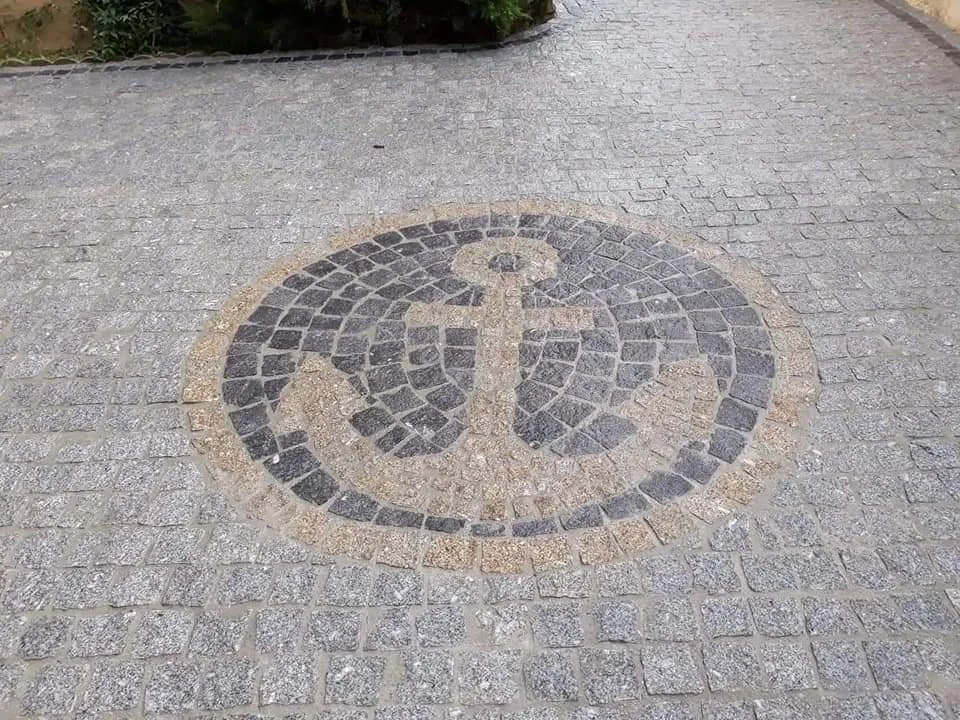 Mosaïque de pierre représentant une ancre dans une zone pavée.