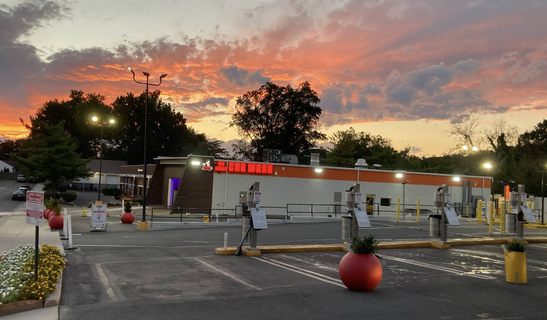 Parking lot outside a restaurant at sunset with vibrant orange and pink clouds in the sky, trees in the background, and some cryptocurrency ATM machines visible.
