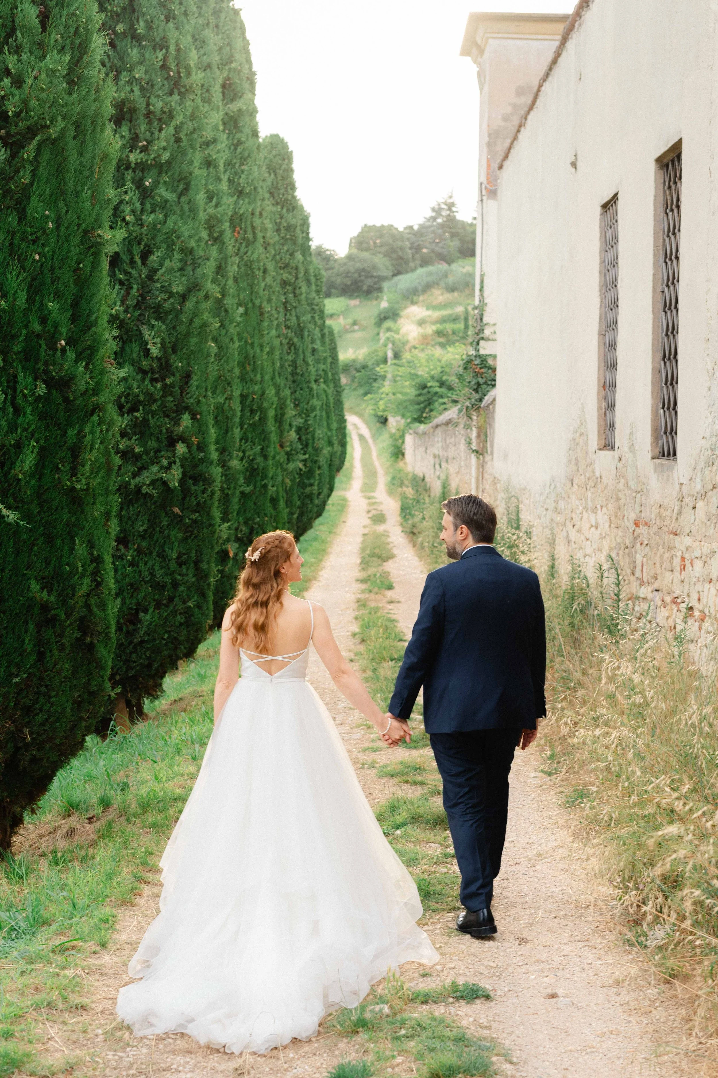 A bride and groom are walking hand in hand down at Villa Mosconi Bertani, Italy.