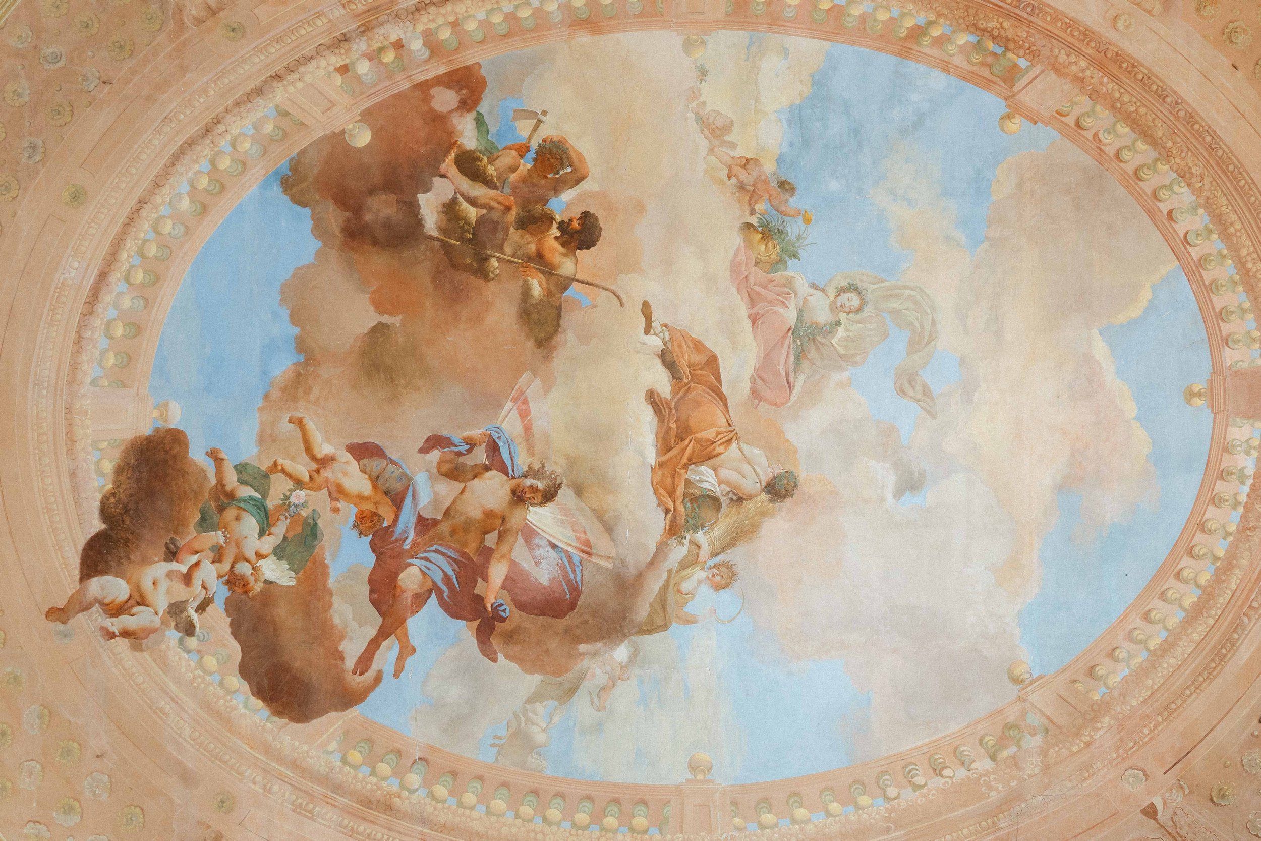 Fresco painting on a dome ceiling depicting mythological figures, including gods, cherubs, and angels, with a bright sky background and decorative architectural details around the border.