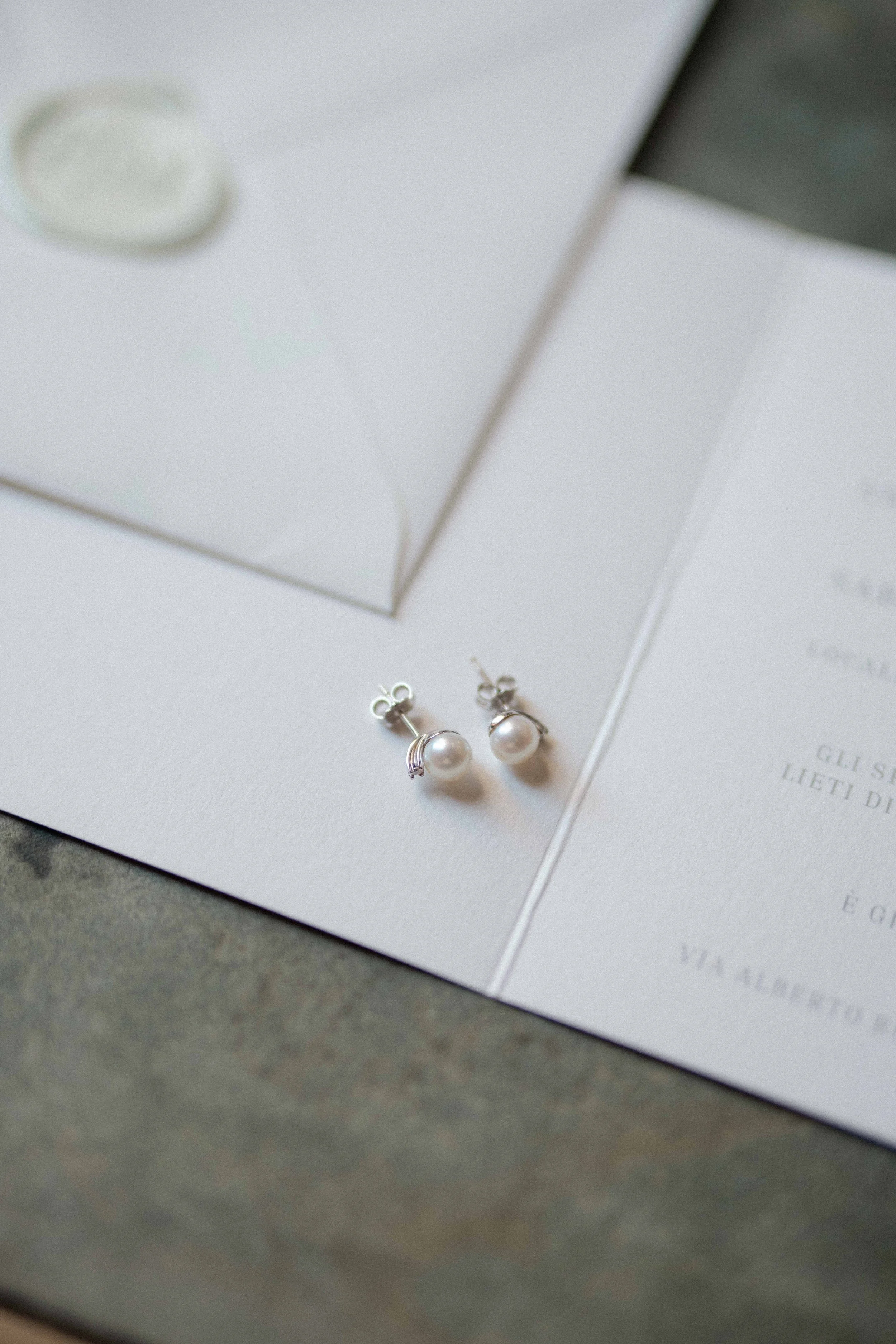 Close-up of pearl earrings on white paper with gray surface background.