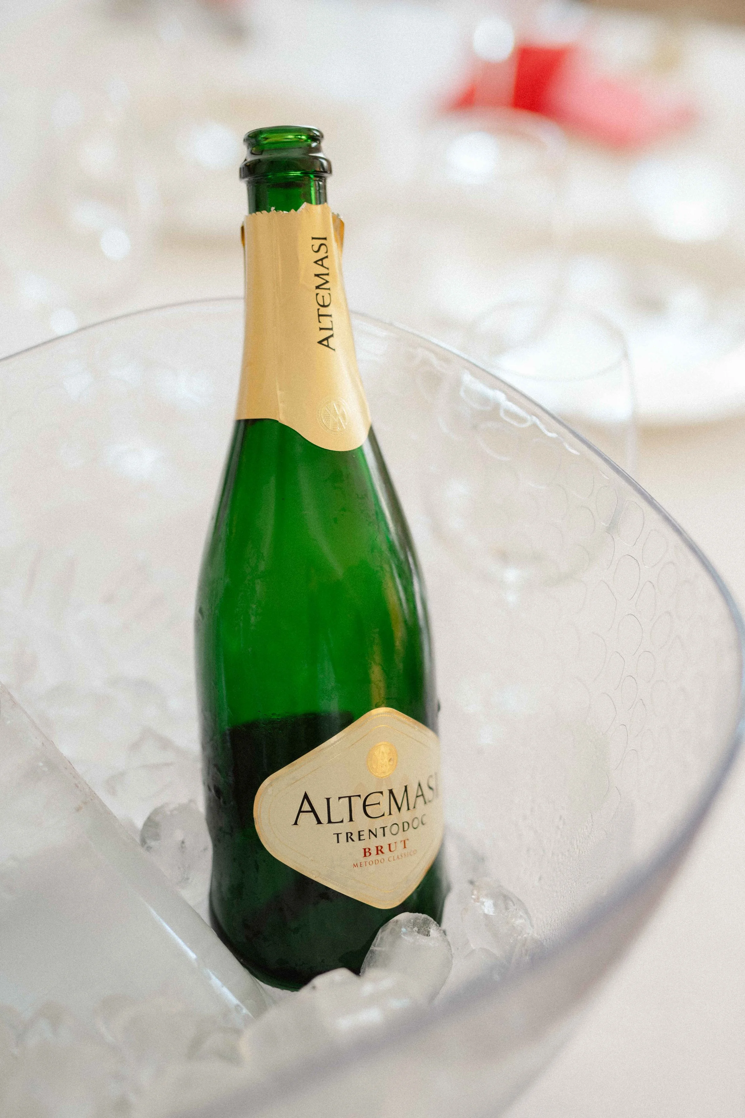 A green bottle of Altemas Trentodoc Brut sparkling wine resting on ice in a metal container.