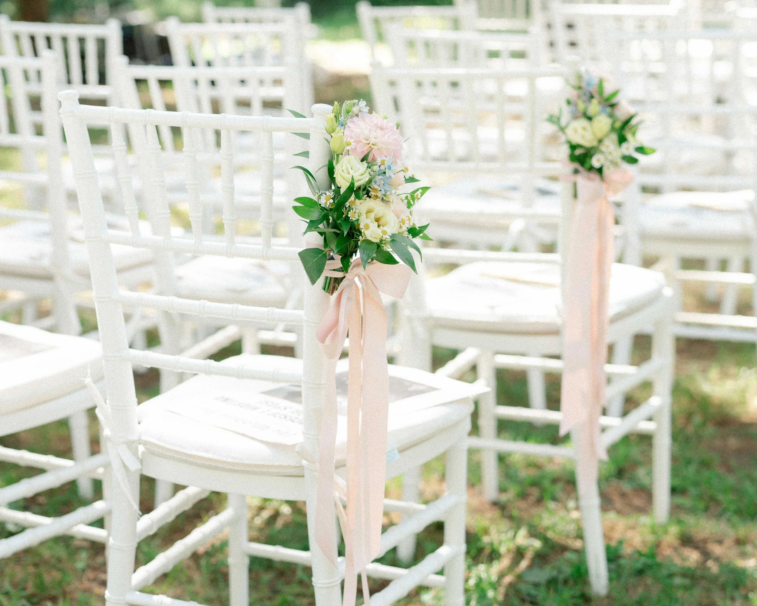 Wedding chairs decorated with flower arrangements along the aisle of an outdoor ceremony.
