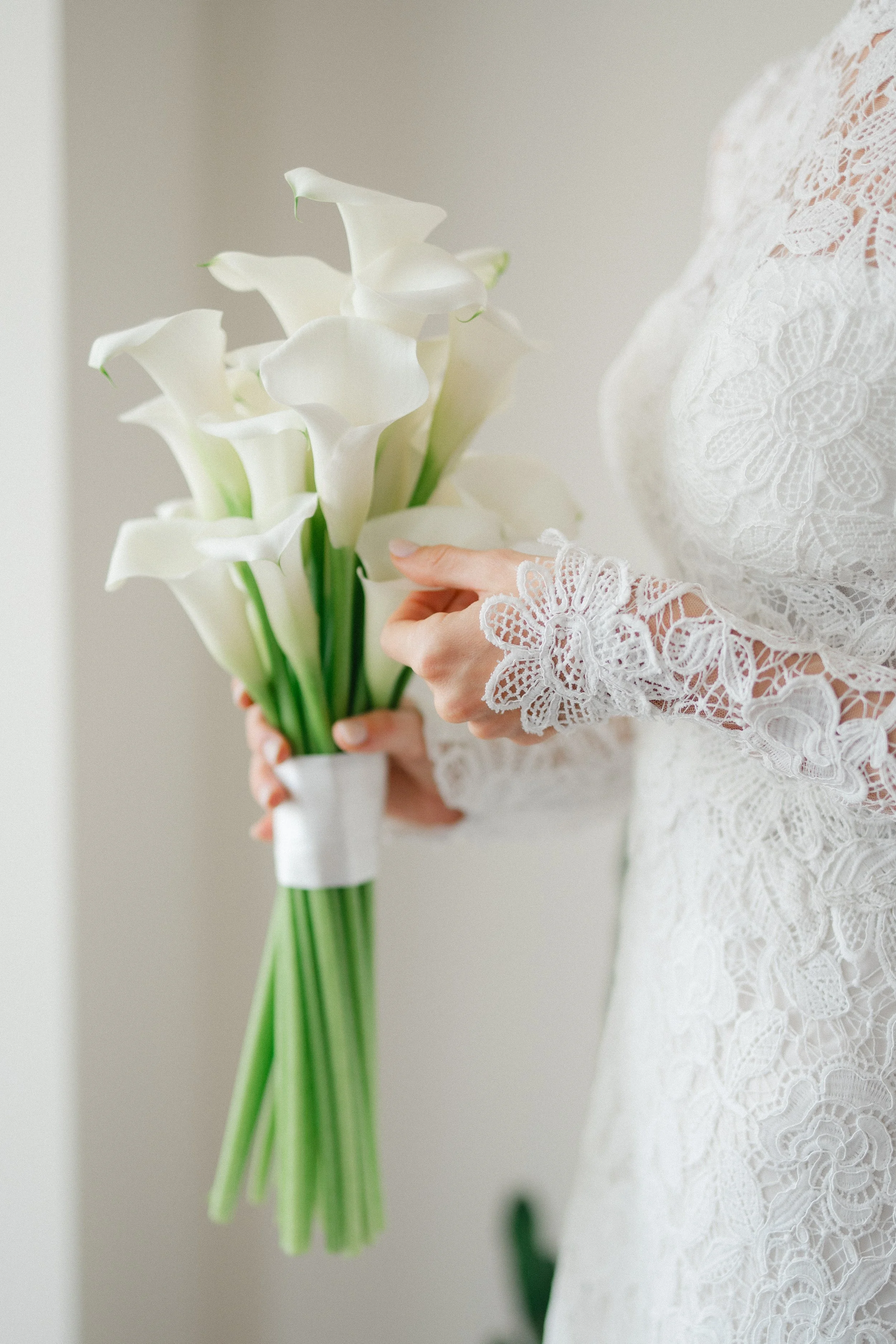 Person in a white lace dress holding a bouquet of white calla lilies.