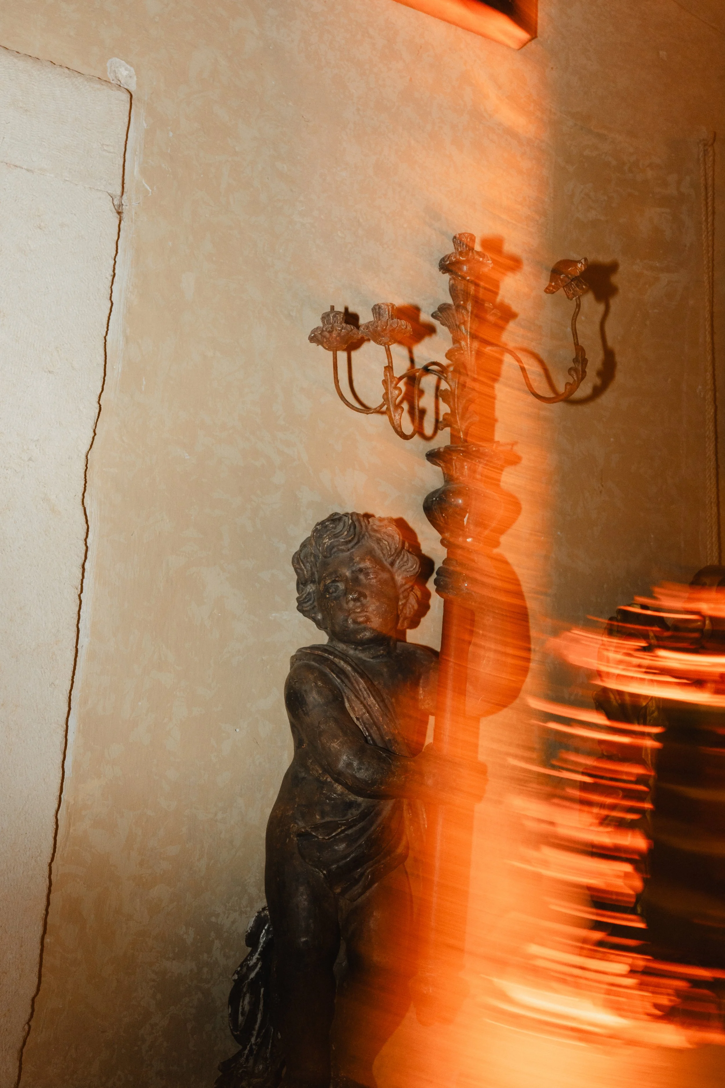 A bronze or dark metal sculpture of a woman with a flowing dress and hair, partially obscured by bright orange light streaks created by a long exposure photograph.