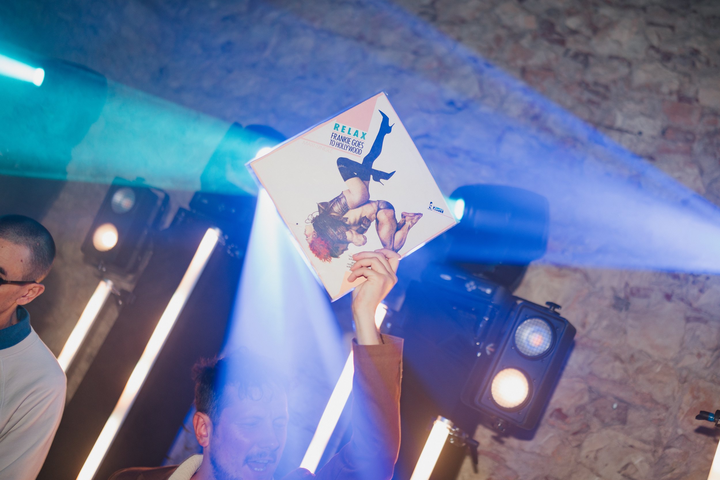 Person holding a magazine featuring a woman's figure on the cover, with blue and purple lighting and people standing nearby.