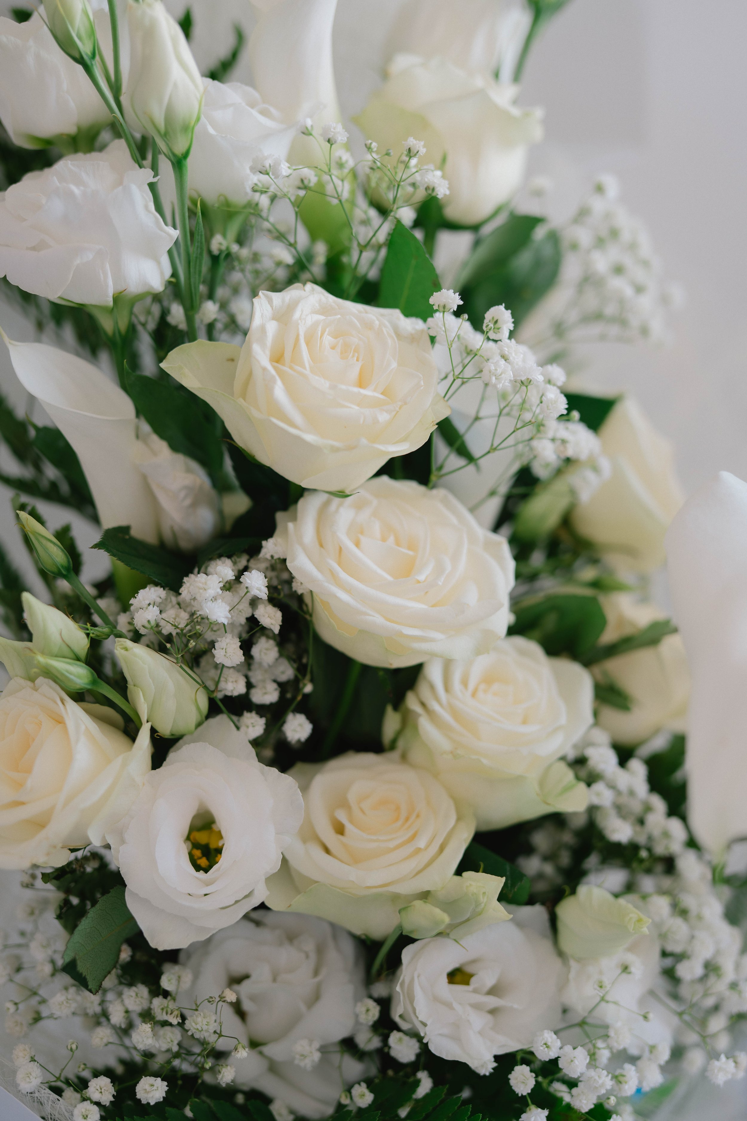 A bouquet of white roses, lisianthus, baby's breath, and assorted greenery.