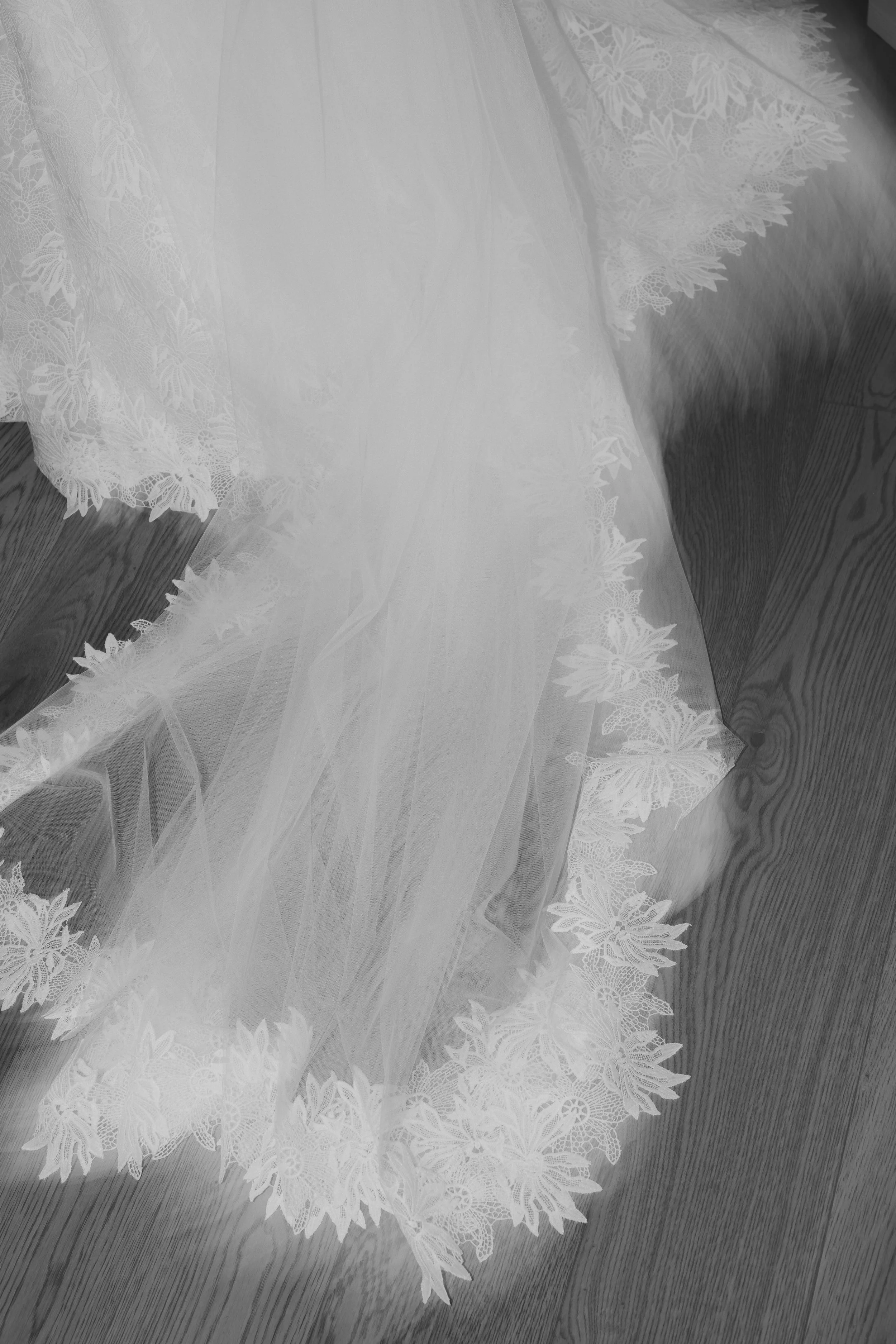 Close-up of a lace wedding veil with intricate floral patterns, draped on a wooden floor.
