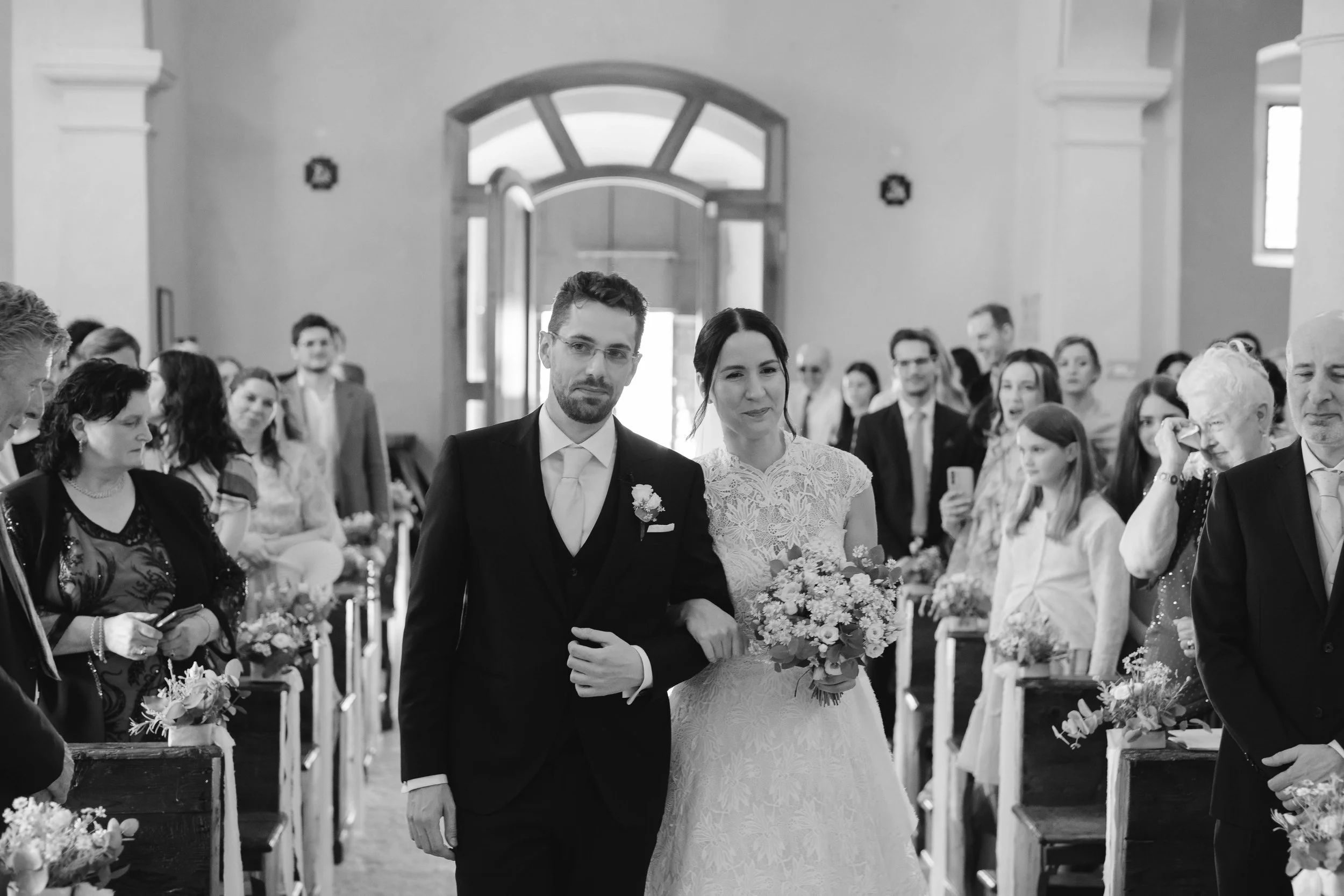 A bride and groom walking down the aisle during a wedding ceremony inside a church, surrounded by guests.