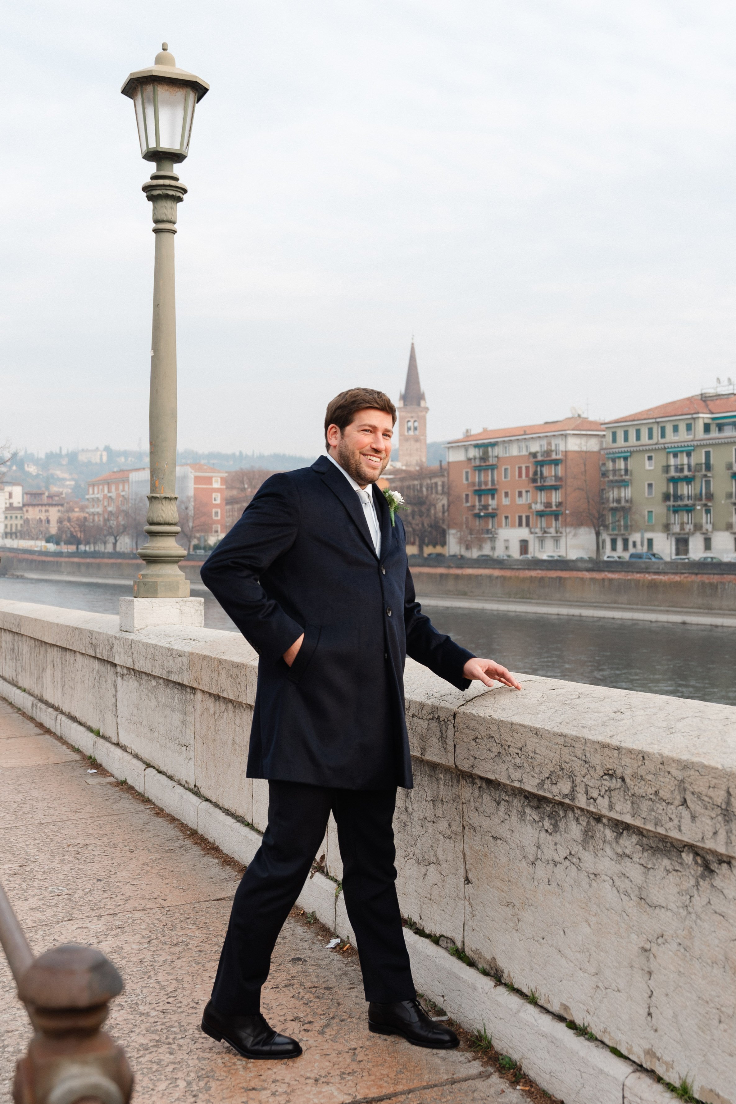 A groom standing by a stone railing on a bridge in Verona, Italy.