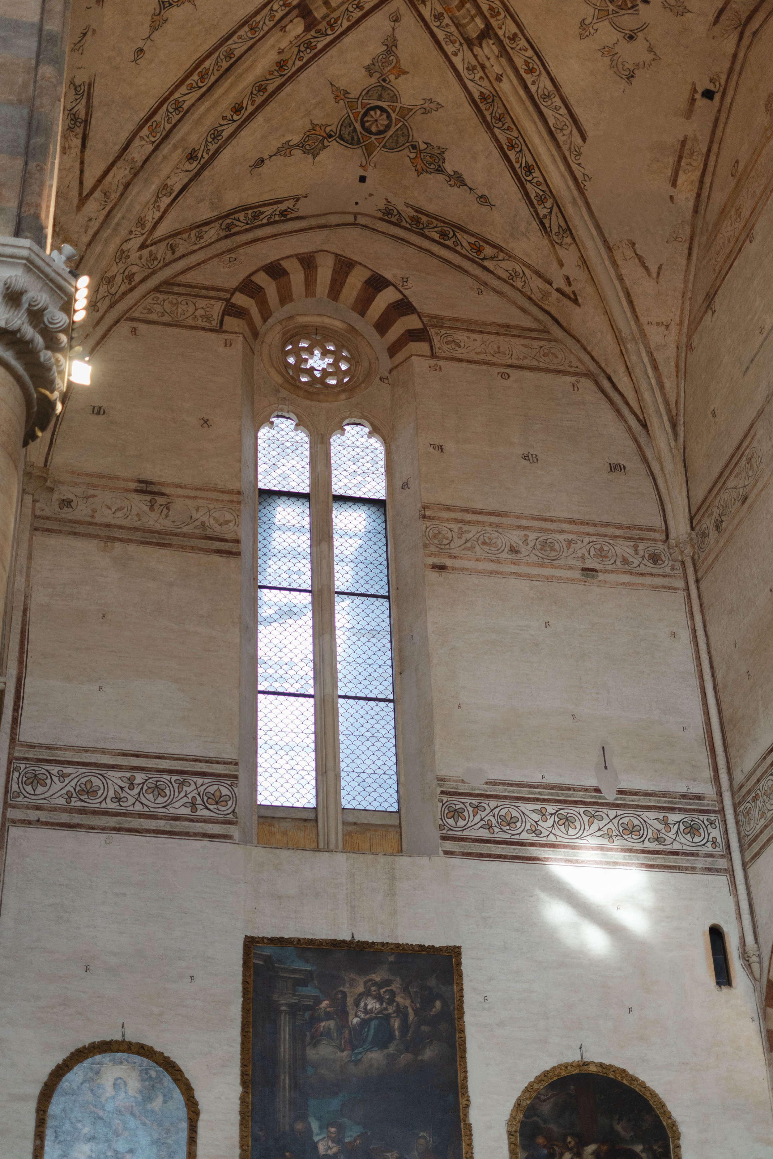 Interior view of a church with a high, decorated ceiling, large stained glass windows, and religious paintings on the walls.