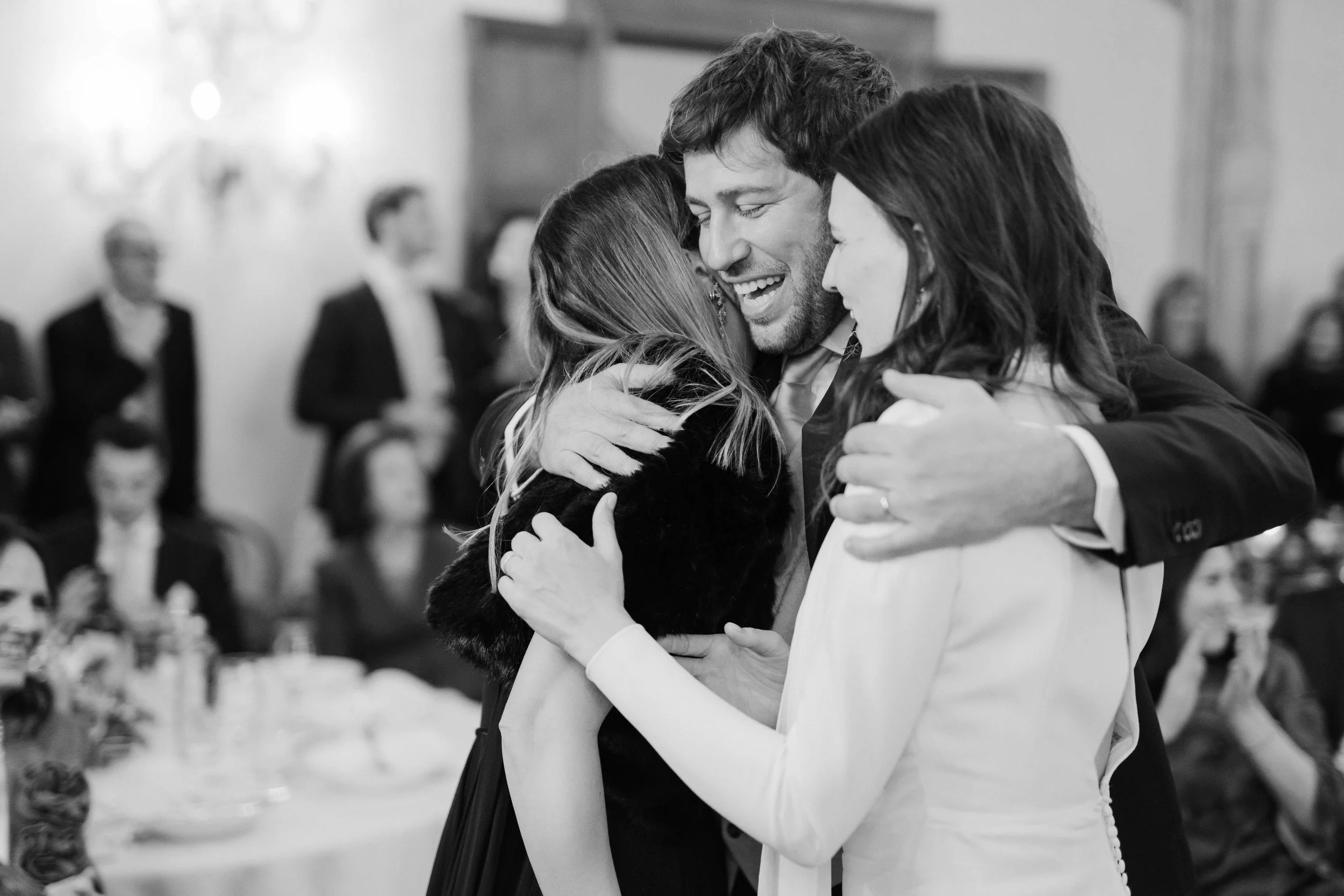 A group of people hug each other at a social event, smiling and celebrating.