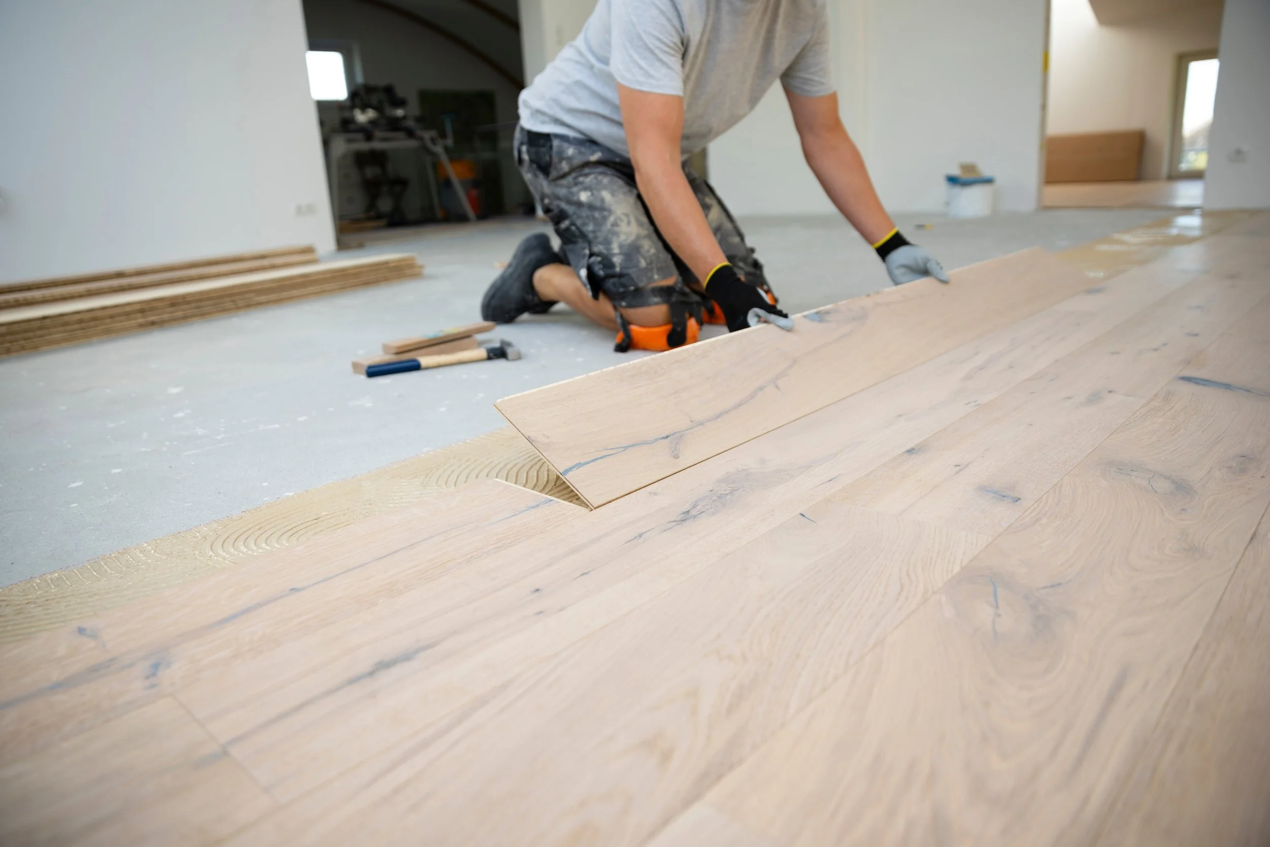 Person installing or working on a hardwood floor in a room with construction tools nearby.