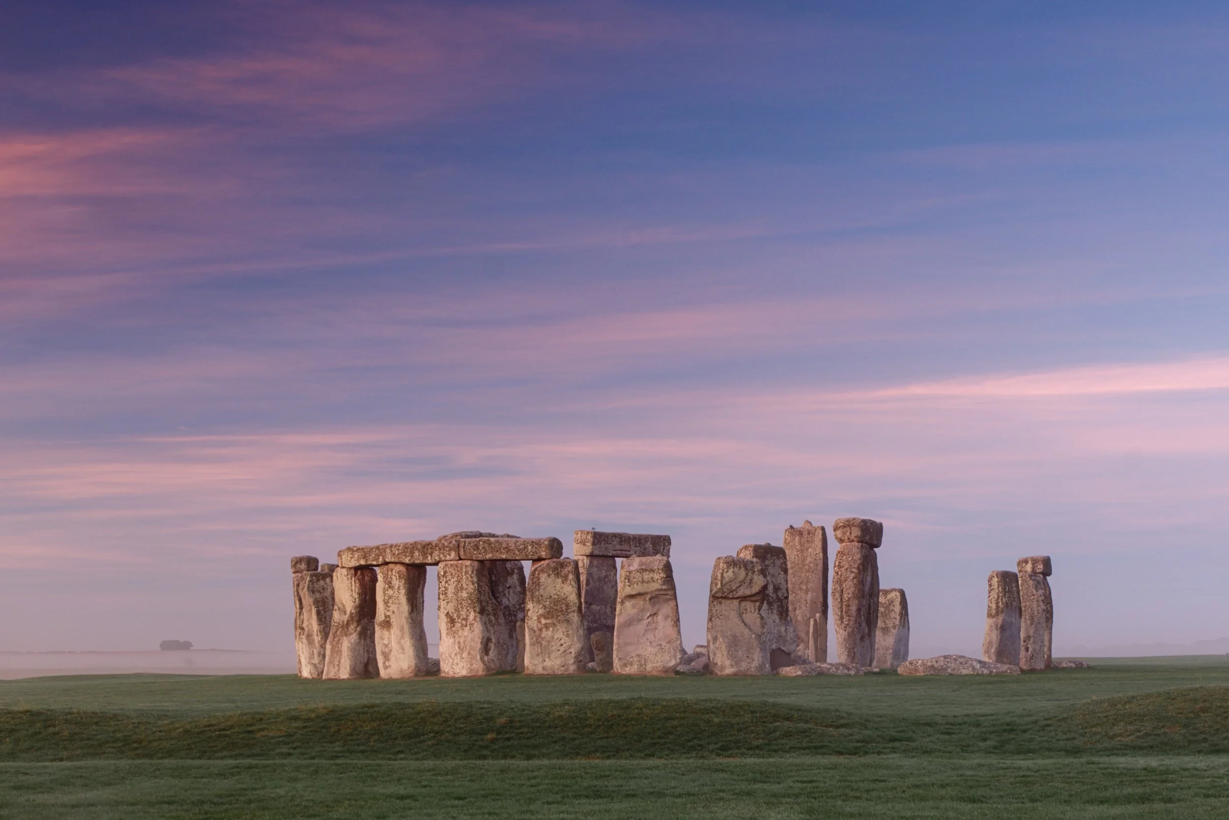 Stonehenge standing stones beneath pink and blue skies with low mist across the Wiltshire landscape