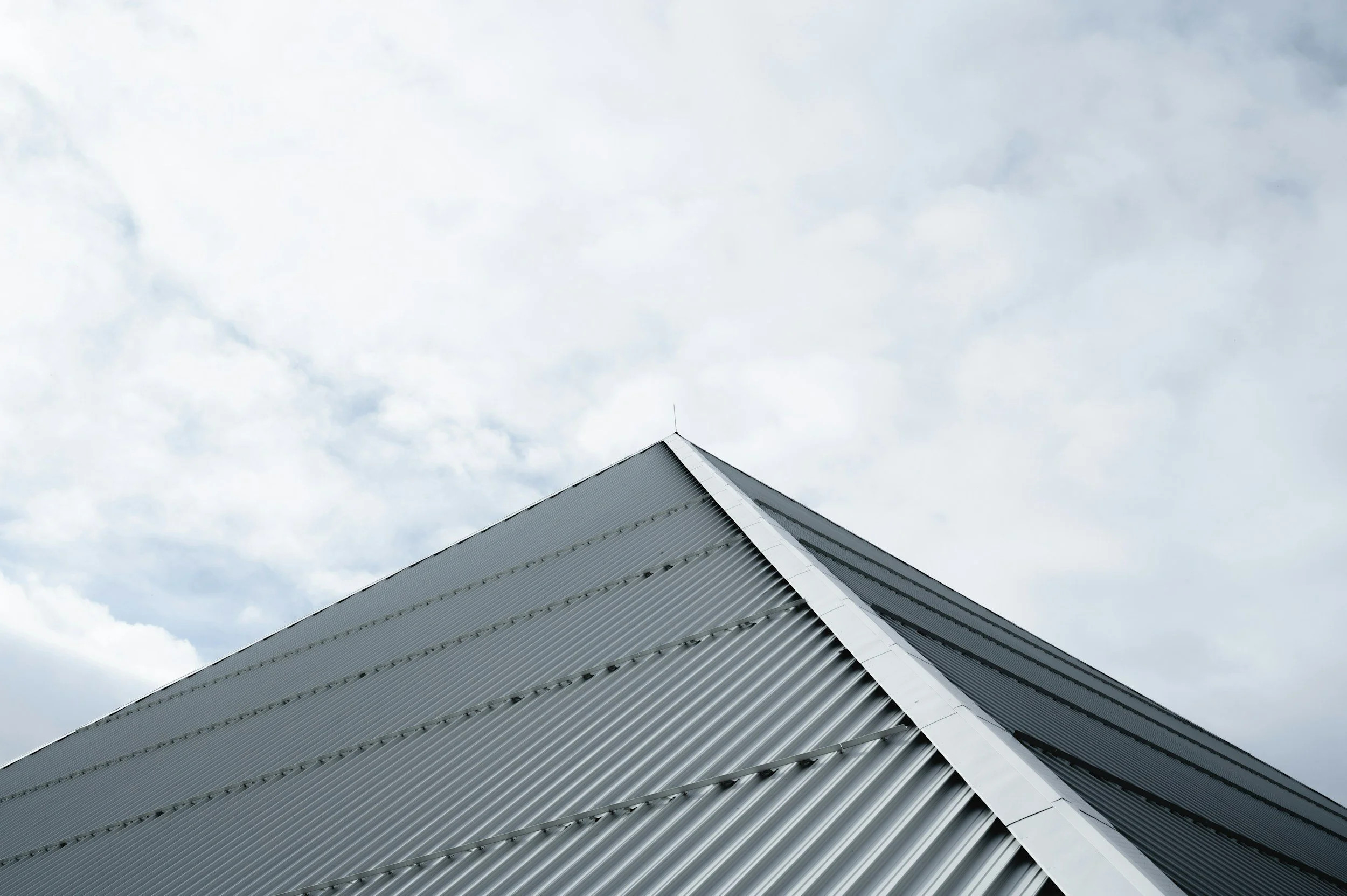 Close-up of a modern, angular building with a metallic, ribbed exterior against a cloudy sky.