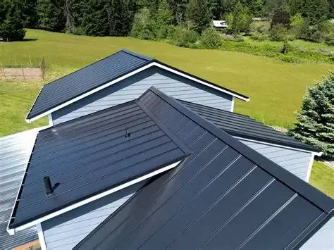 Close-up of three different metal roofs with varying angles and colors on residential buildings, with a grassy yard and trees in the background.