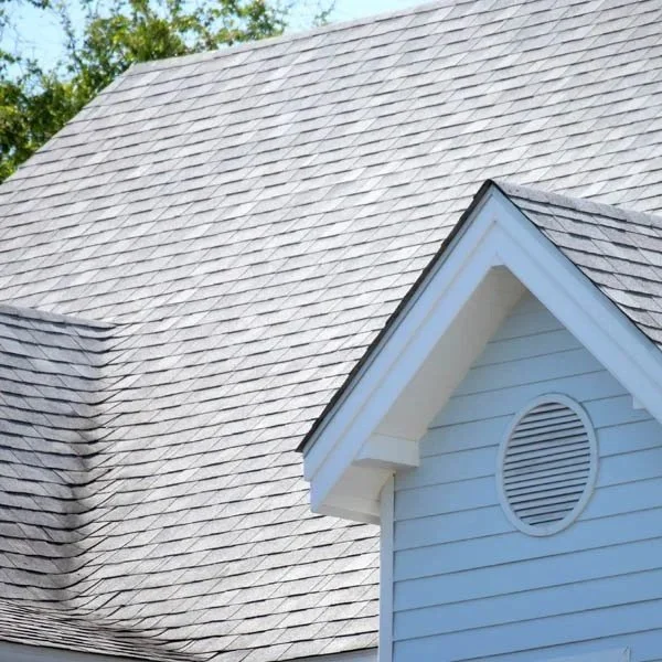 Close-up of a residential house's roof with gray shingles and part of the white exterior wall with an air vent.