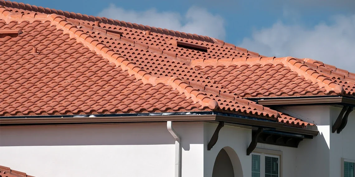 Close-up of a house roof with red clay tiles and a cloudy sky in the background.