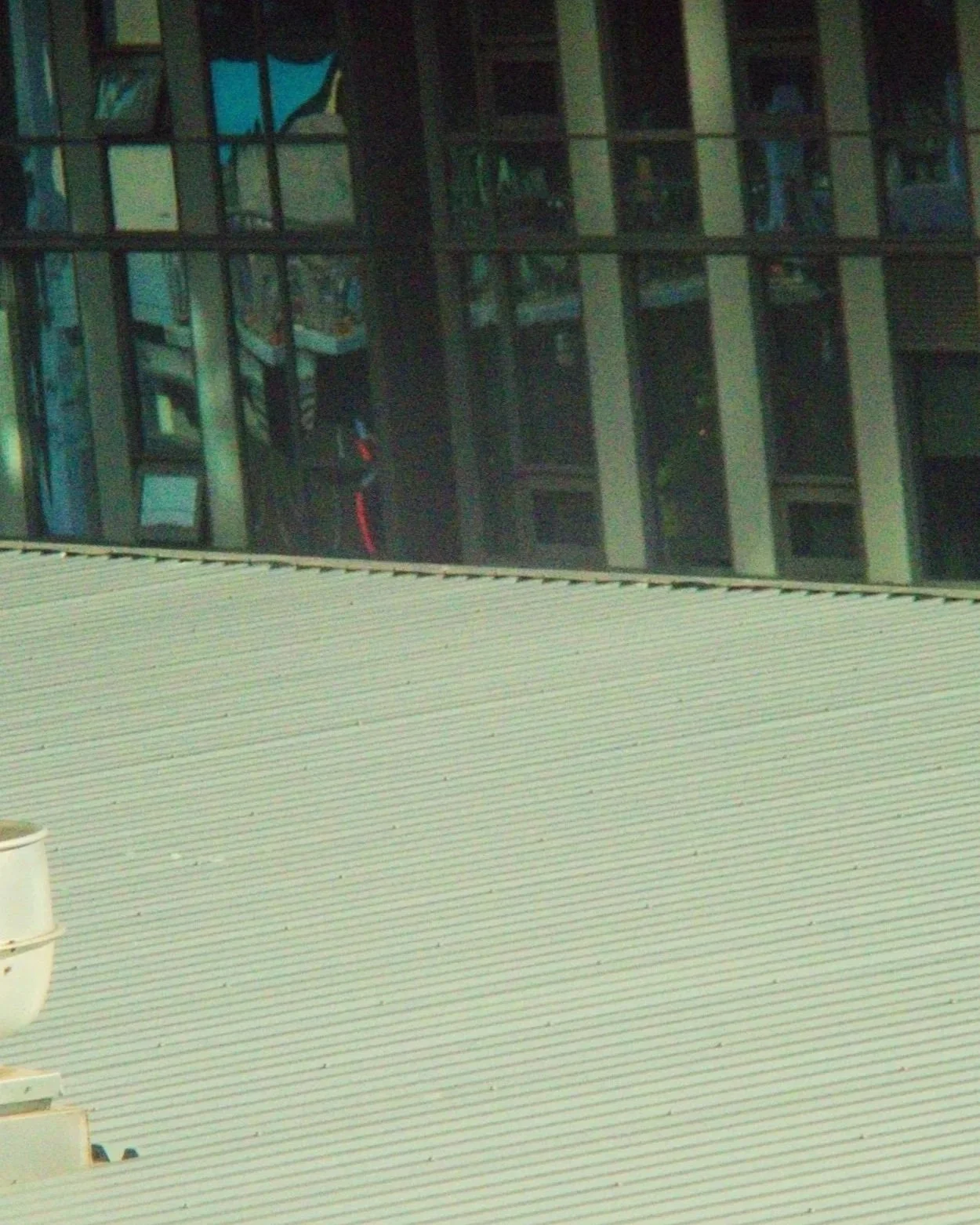 View of a building with several floors, reflecting neighboring buildings in windows, with a beige-colored roof in the foreground.