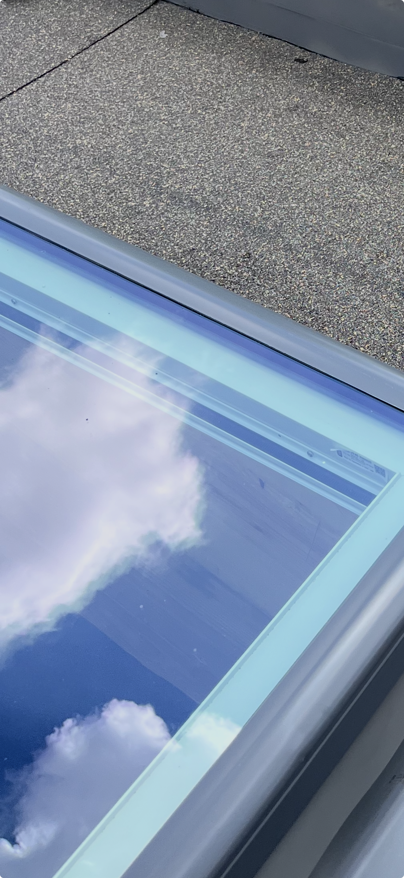 View of cloudy sky reflected in a glass surface, with part of a concrete ground visible at the top of the image.