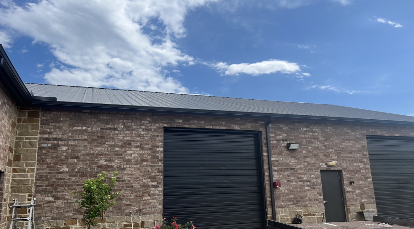 Brick building with two black garage doors, a small door, an outdoor light, and a blue sky with clouds.