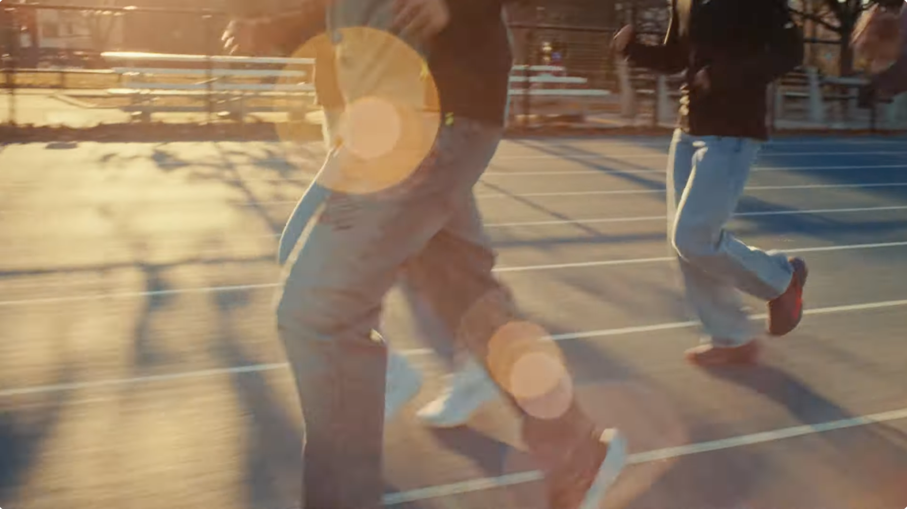 People jogging on a parking lot during sunset, with trees and a fence in the background.