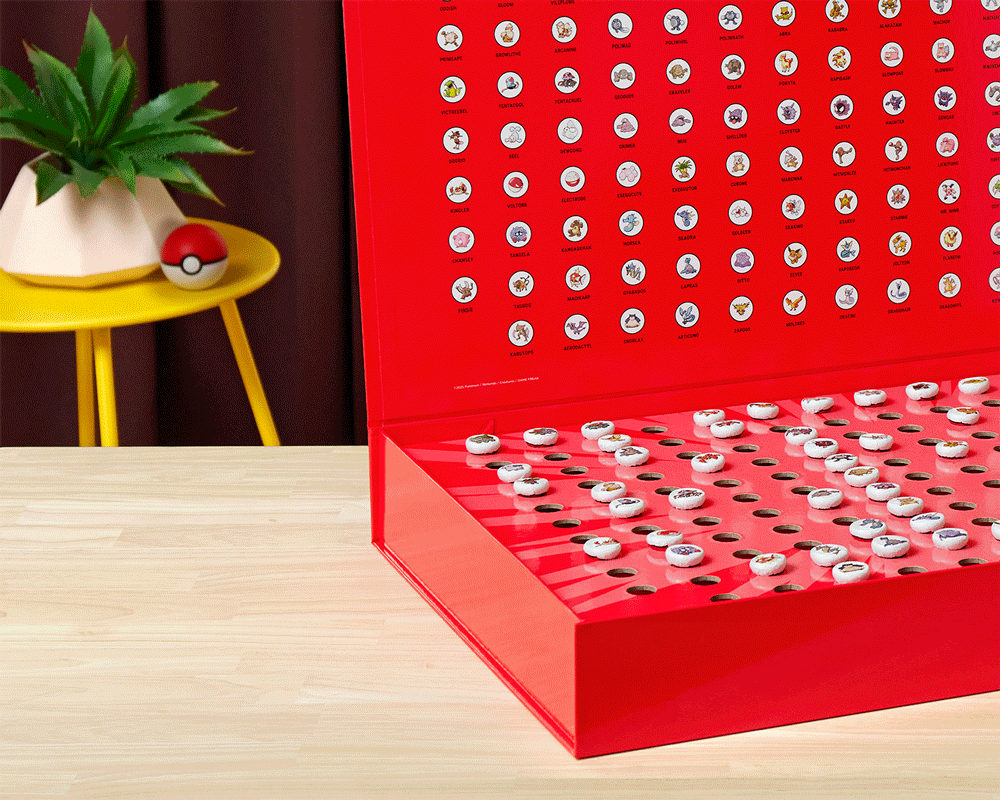 A red tin box with illustrations of Pokémon characters on the inside lid and small Pokémon-themed candies in the bottom compartment.