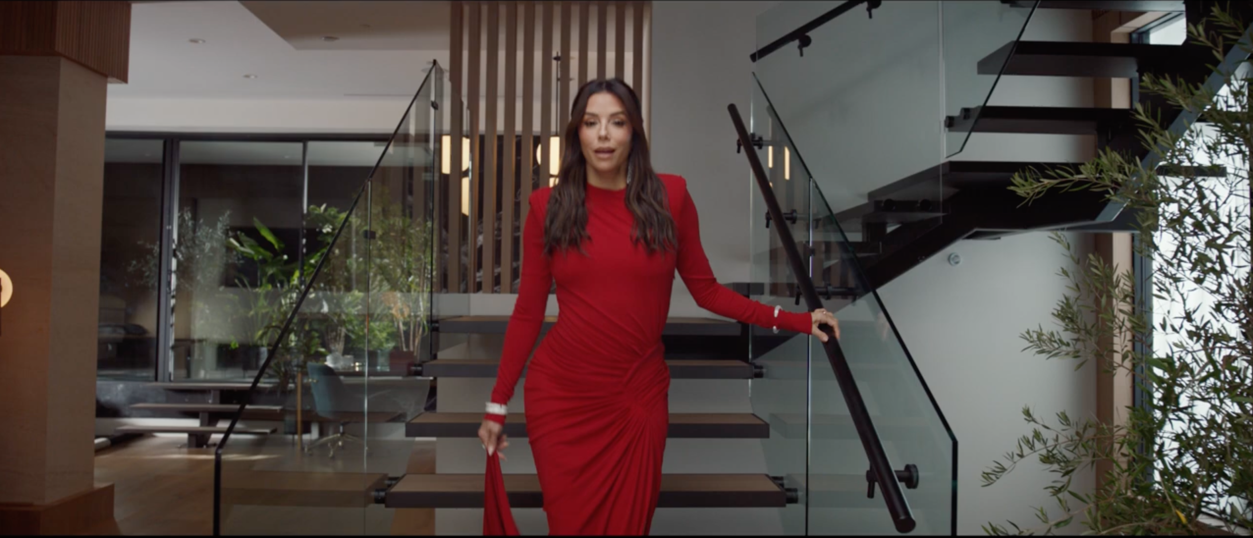 Eva Longoria walking down a modern staircase in a contemporary home interior.