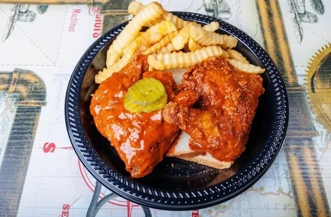 Fried chicken, French fries, and a pickle on a sandwich bun in a black plastic basket