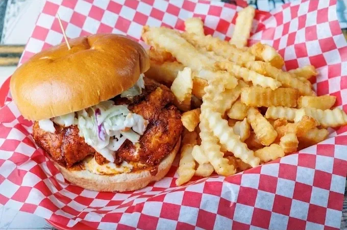 Fried chicken sandwich with coleslaw in a bun, served with crinkle-cut French fries on red and white checkered paper