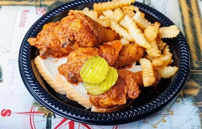 Fried chicken with pickles, served on bread with crinkle-cut fries on a black tray.