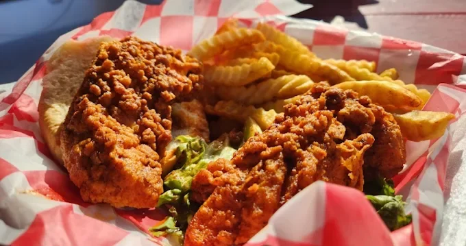 Fried chicken tenders with crinkle-cut French fries in a basket lined with red and white checkered paper.
