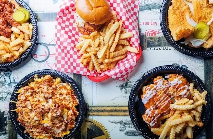 Four takeout containers with food surrounding a small burger and fries in a basket.