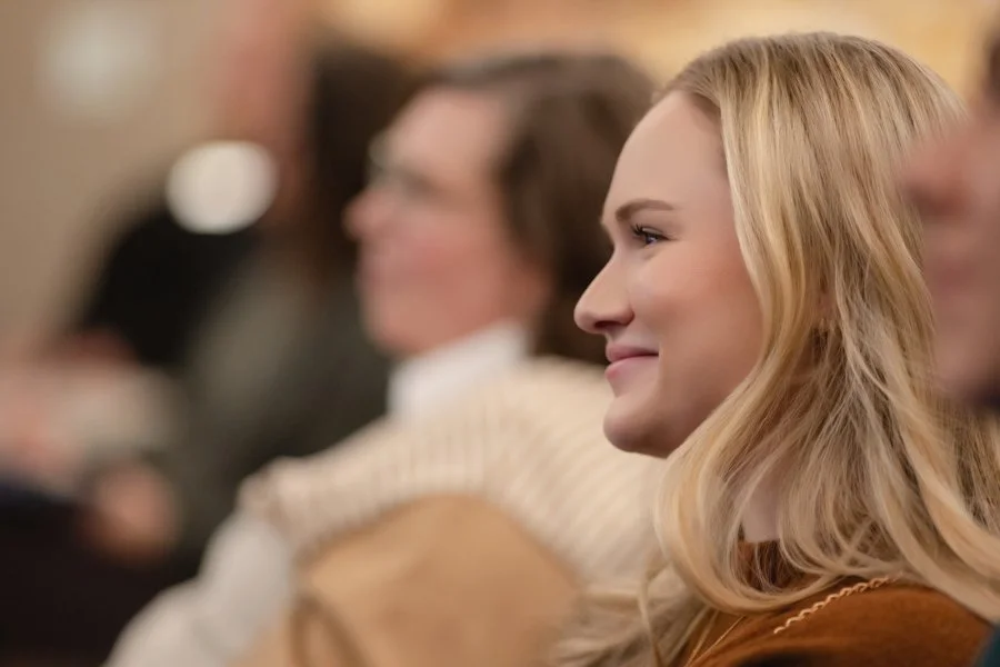 A woman with blonde hair smiling while sitting in a crowded room watching presenters at the Women's Small Business Expo in Redmond, WA.