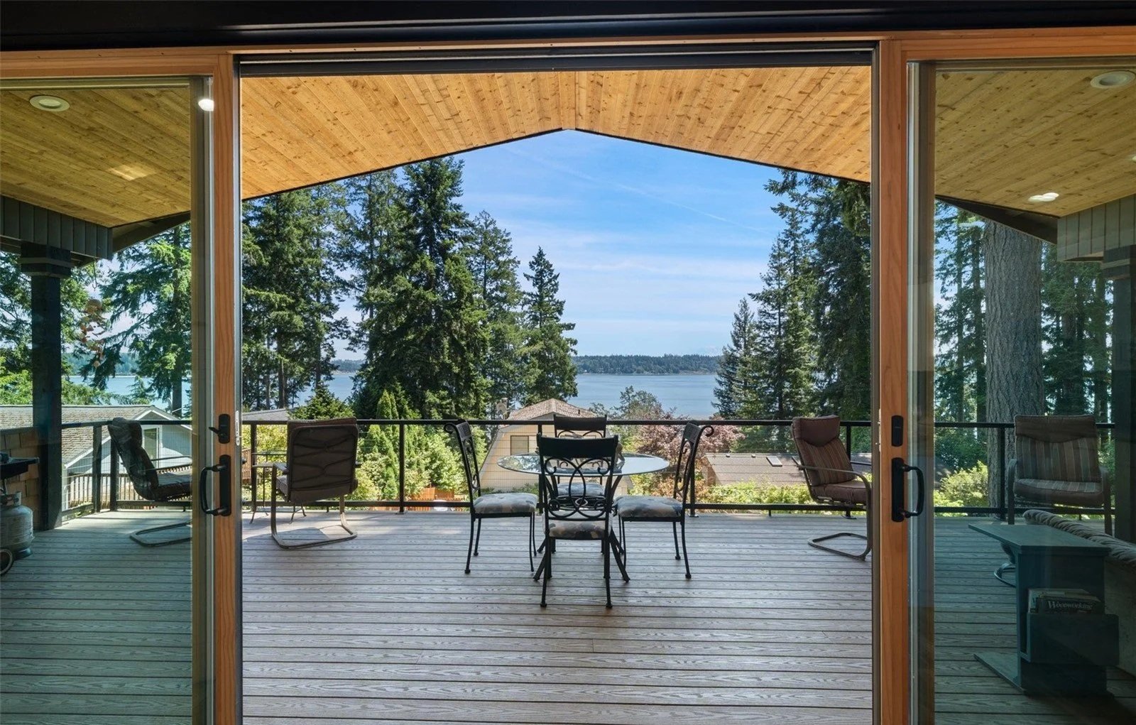 View of a balcony overlooking trees and a body of water, with outdoor chairs and a informational stand.