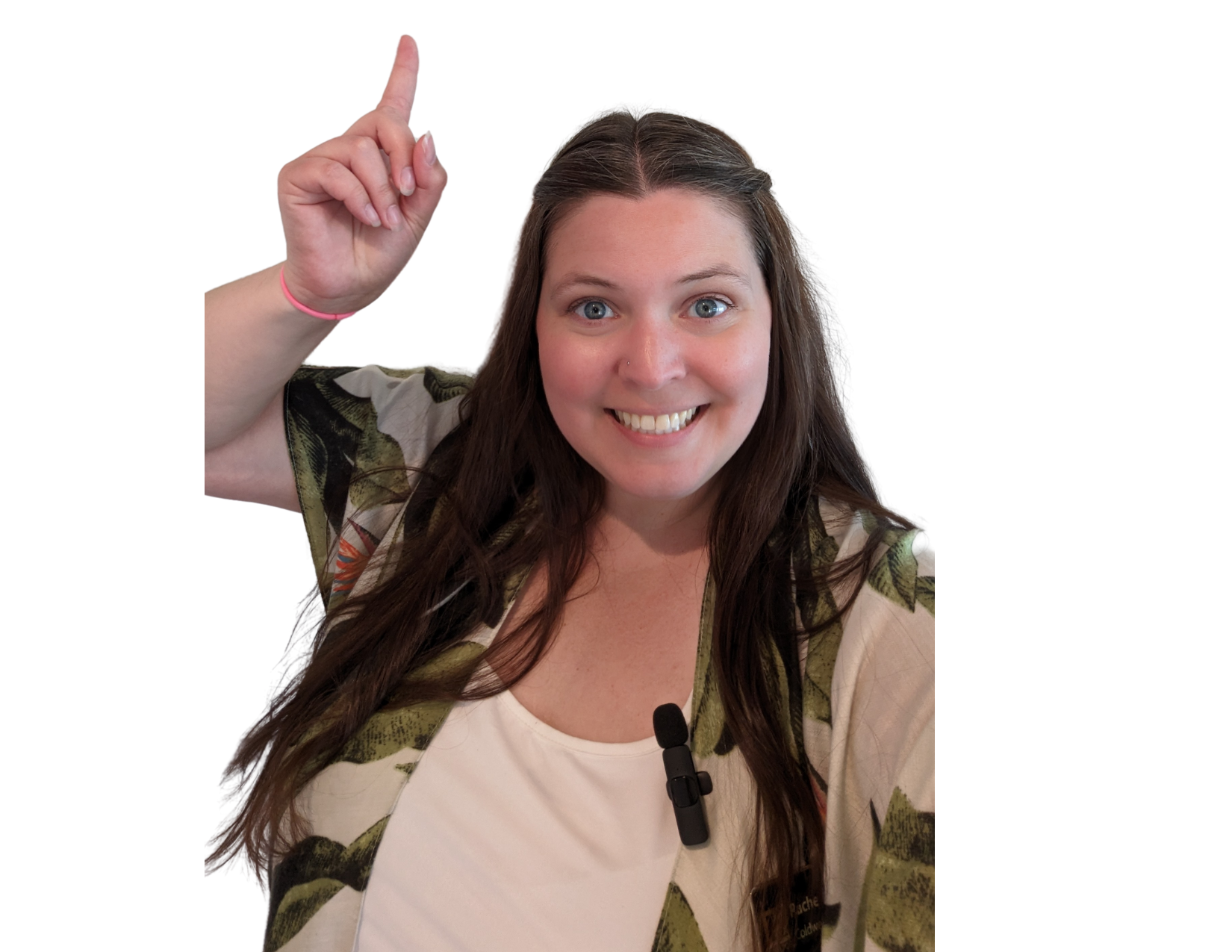 Smiling woman with long brown hair, wearing a white top and a floral-patterned jacket, points upward with her right index finger, and has a microphone clipped to her shirt.