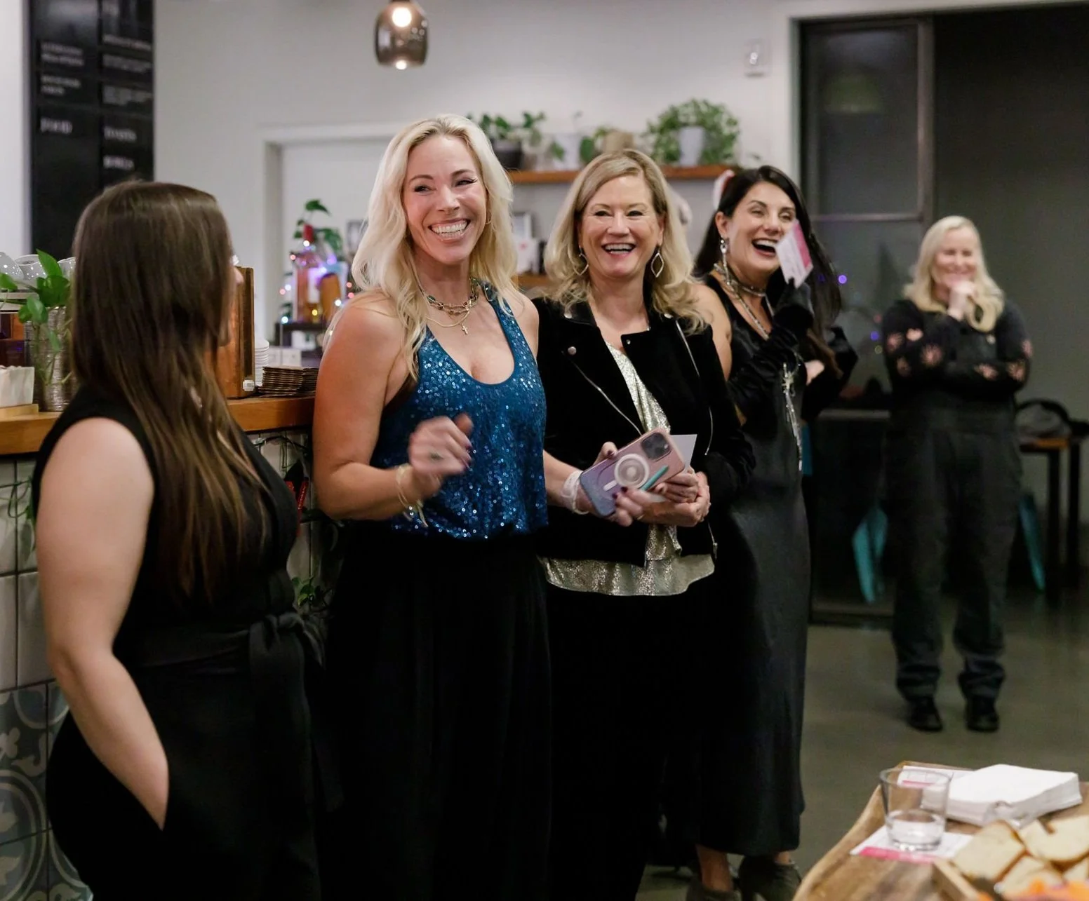 A group of women standing in a line laughing and smiling at a holiday party at Bellden Cafe in Bellevue, Washington.