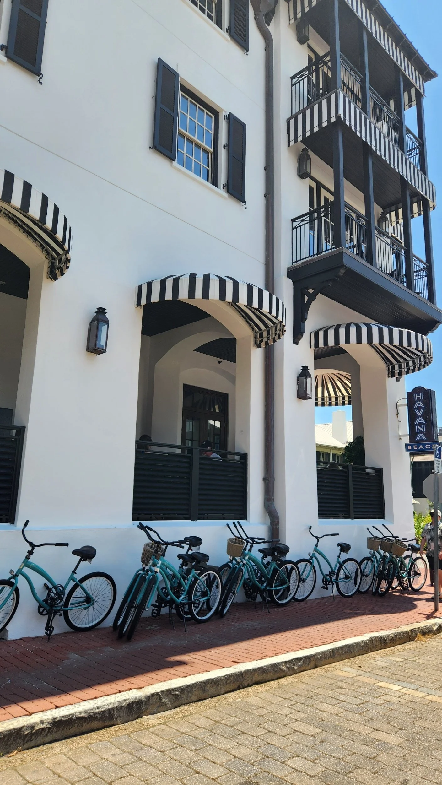 Havana Beach hotel facade with black-and-white striped awnings, balconies, and turquoise rental bicycles