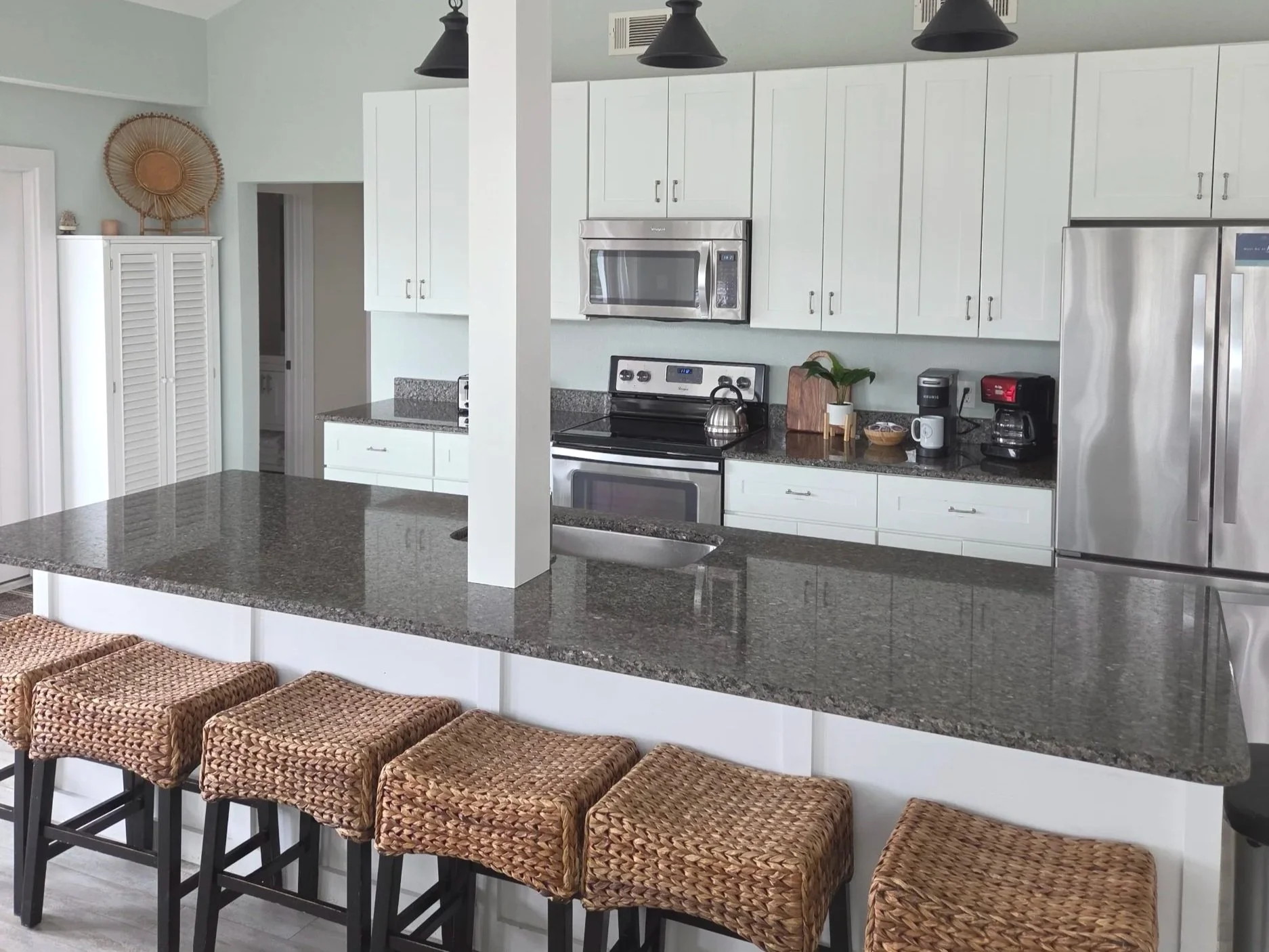 Bright modern kitchen with white cabinets, granite countertops, stainless steel appliances, island bar, and woven wicker stools