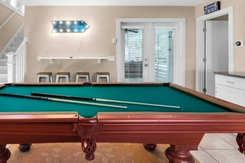 Green billiards table with pool cues in a beach-themed game room