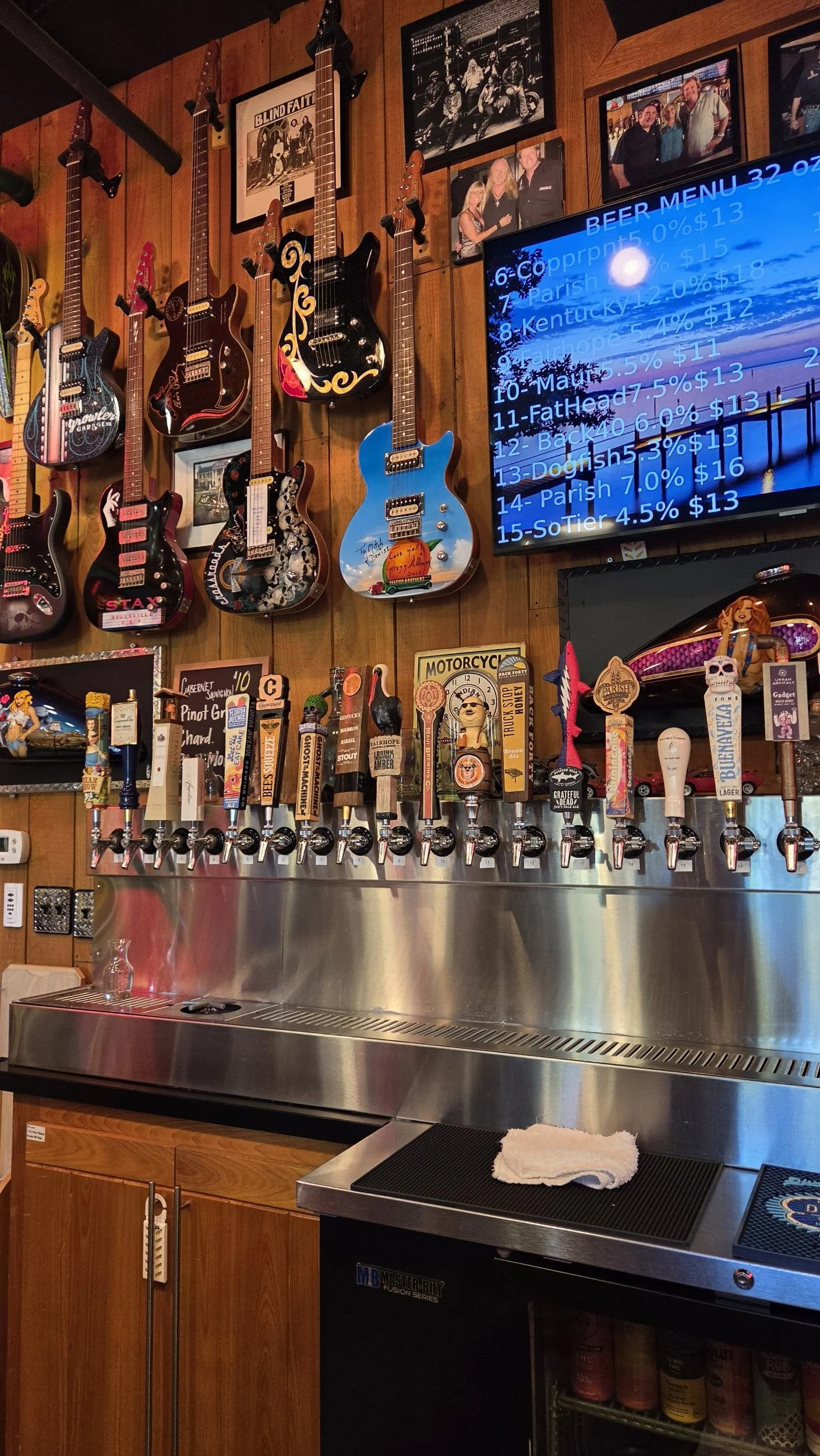 Craft beer bar with numerous beer taps, mounted electric guitars, framed band photos, and a digital beer menu.