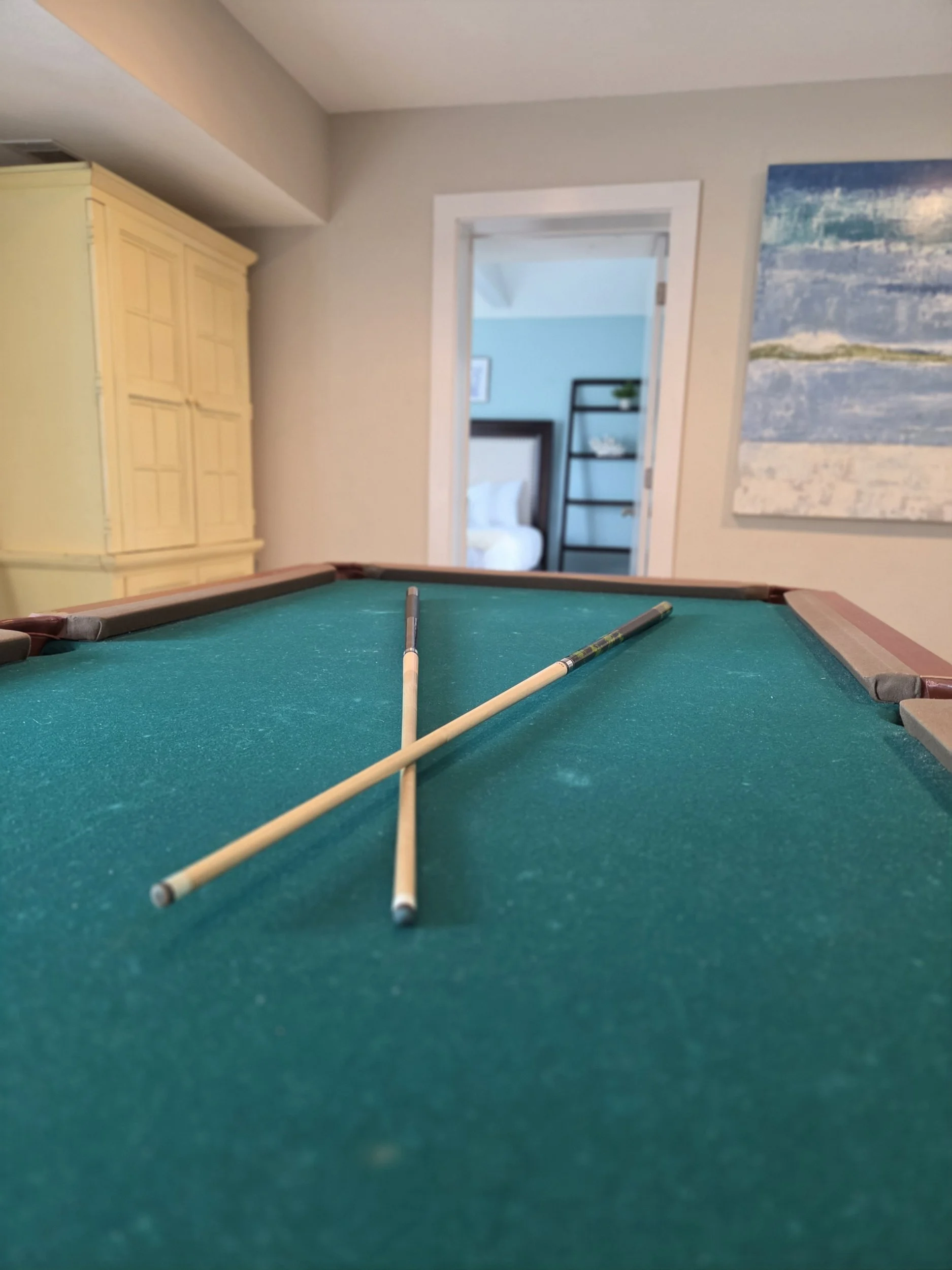 Green-felt pool table with two billiard cues in a home game room