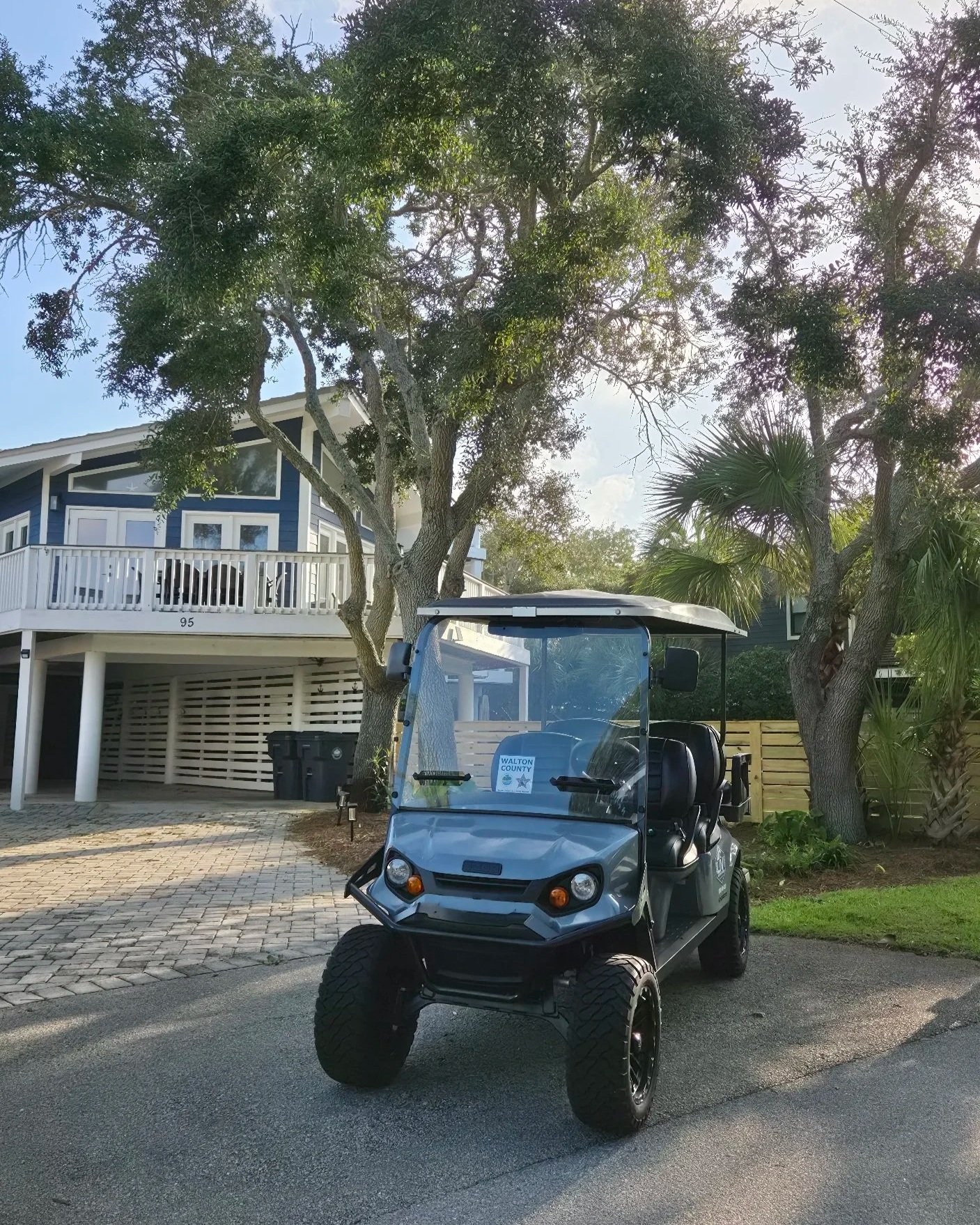 Blue golf cart parked in front of a coastal-style house surrounded by palm trees